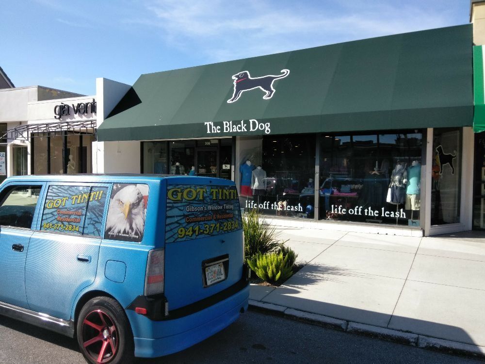 Blue delivery van parked outside The Black Dog store with a green awning and sidewalk display windows
