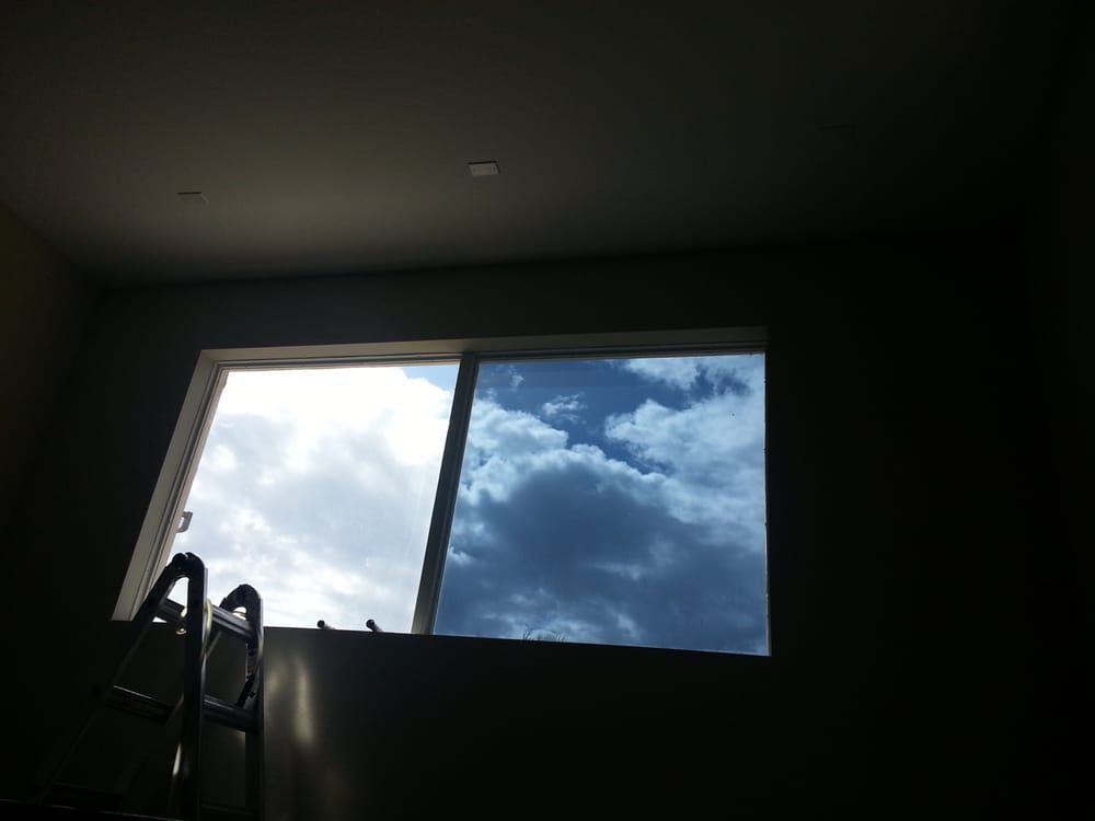 Dim room with a bright window showing blue sky and clouds, and a ladder in the foreground.