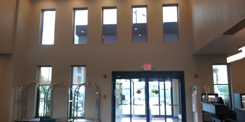 Lobby with tall windows, glass entrance doors, and wood-paneled walls, lit by daylight.