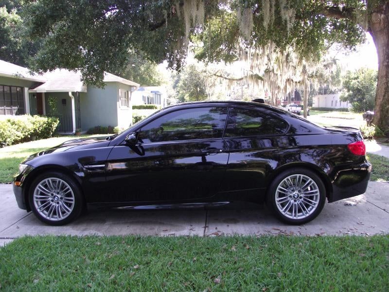 Black sedan parked on a grassy curbside under a tree in a residential neighborhood