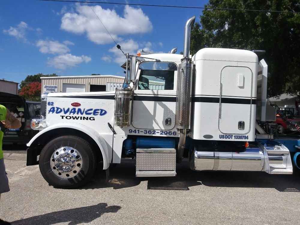 White tow truck parked outdoors with blue “Advantage Towing” lettering and clear blue sky background