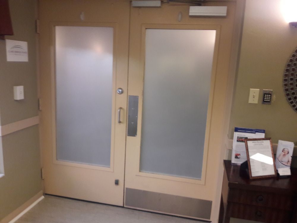 Closed double doors with frosted glass panels in a hallway near a wall-mounted sanitizer dispenser.