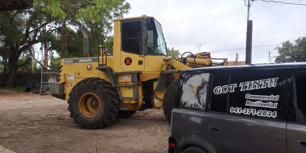 Yellow construction loader beside a black van on a dirt roadside