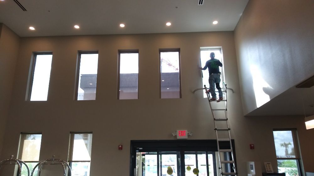 Person on a ladder changing a light in a tall lobby with high windows and glass doors