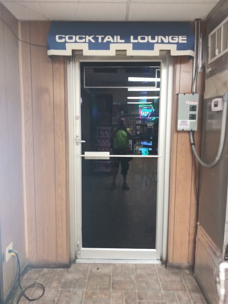 Entrance to a cocktail lounge with a glass door, neon sign, and tiled floor.