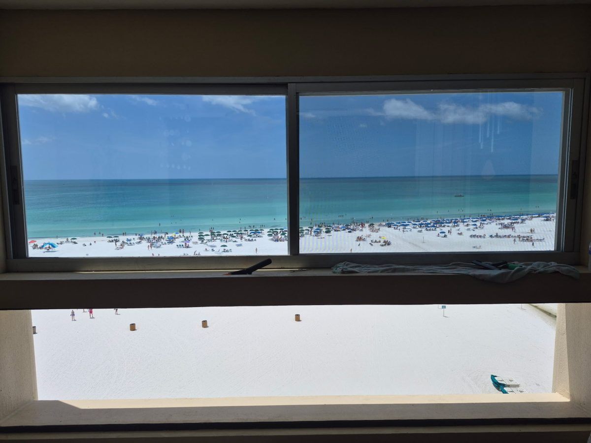 Ocean view through a window with blue sea and white sandy beach below.