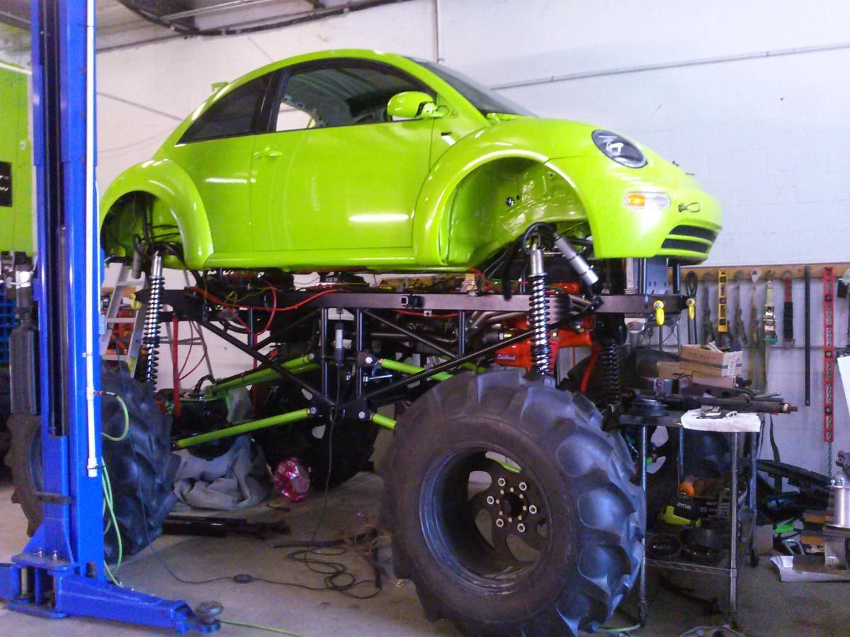 Bright lime green off-road buggy with oversized tires in a workshop lift, viewed from below