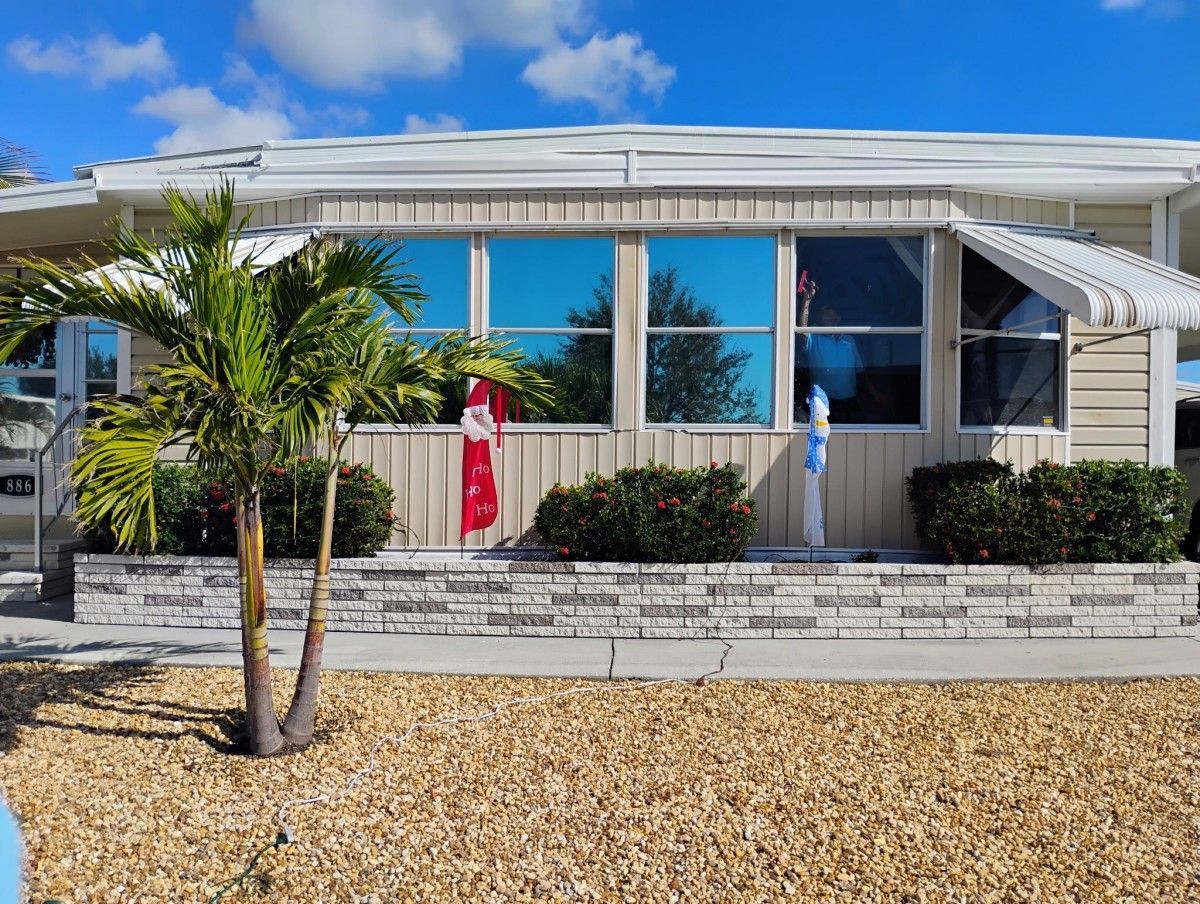 Front view of a white building with palm trees, a red flag, and a gravel courtyard under a blue sky