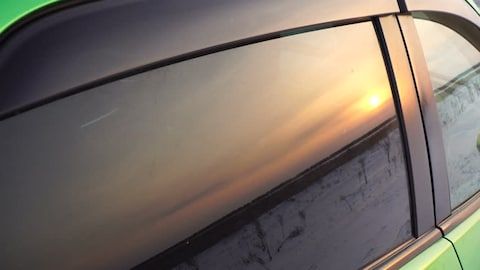 Sunset reflected on a car’s dark tinted side window with black trim.