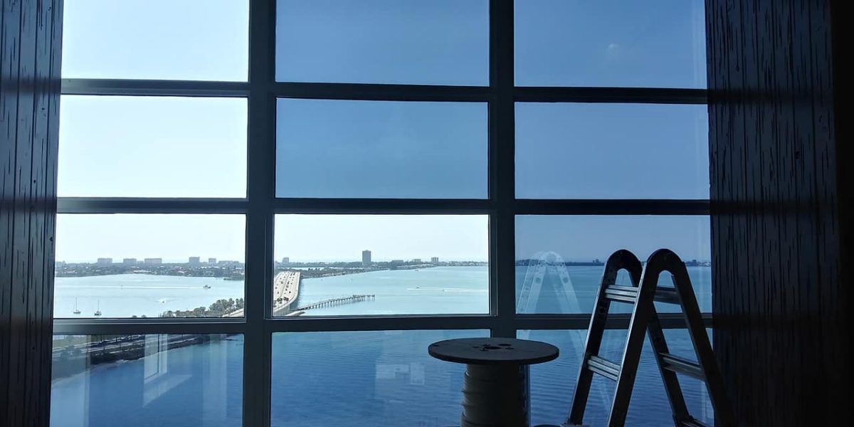 Snowy waterfront view through large windows, with a ladder and small table in the foreground