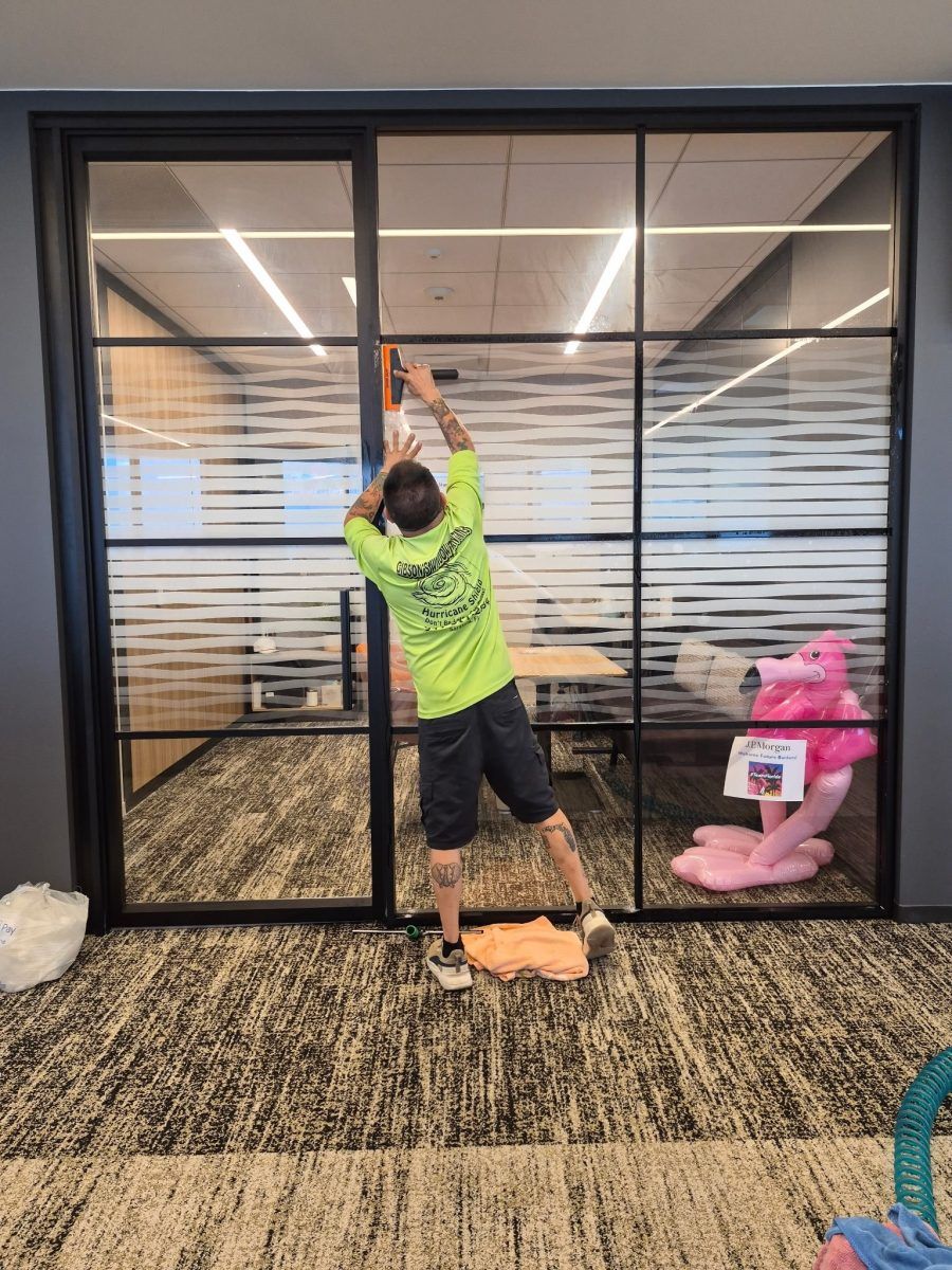 Person in neon green shirt uses a long pole to clean a glass office wall.