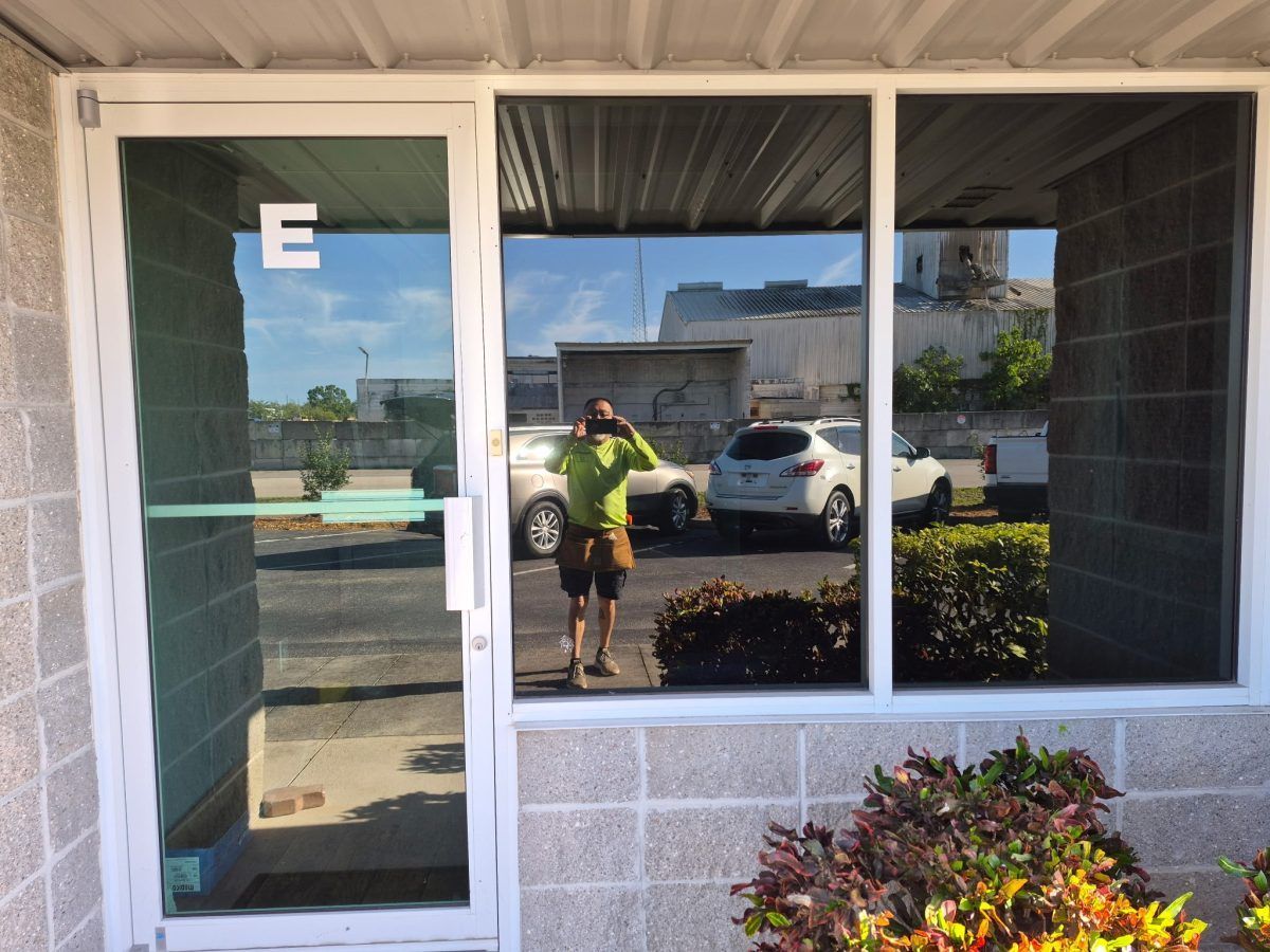 Storefront window reflecting a person in a neon shirt standing outside near parked cars