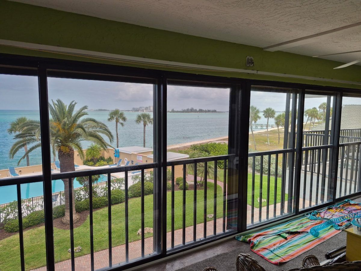 Balcony view of a beach resort with palm trees, ocean, and patio railing at sunset