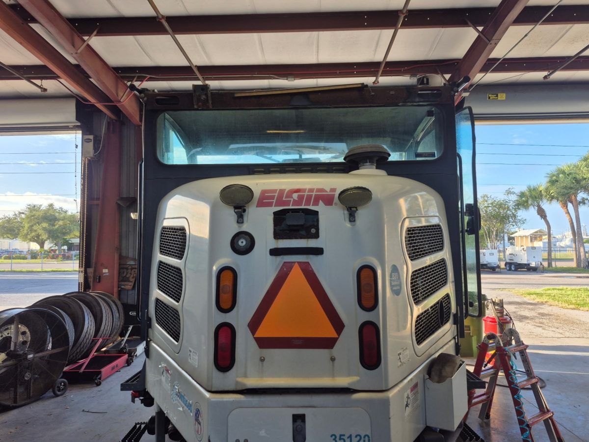 Rear view of a white utility vehicle with orange hazard triangle, parked under a metal roof.