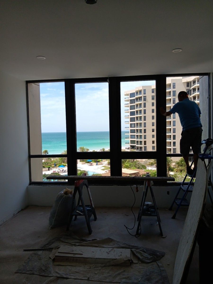 Person installing a large window in a room with ocean and high-rise views beyond.