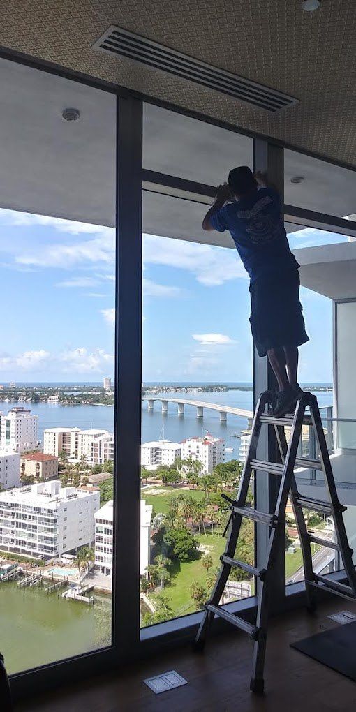Worker standing on a ladder cleaning or installing a large window with a city view outside