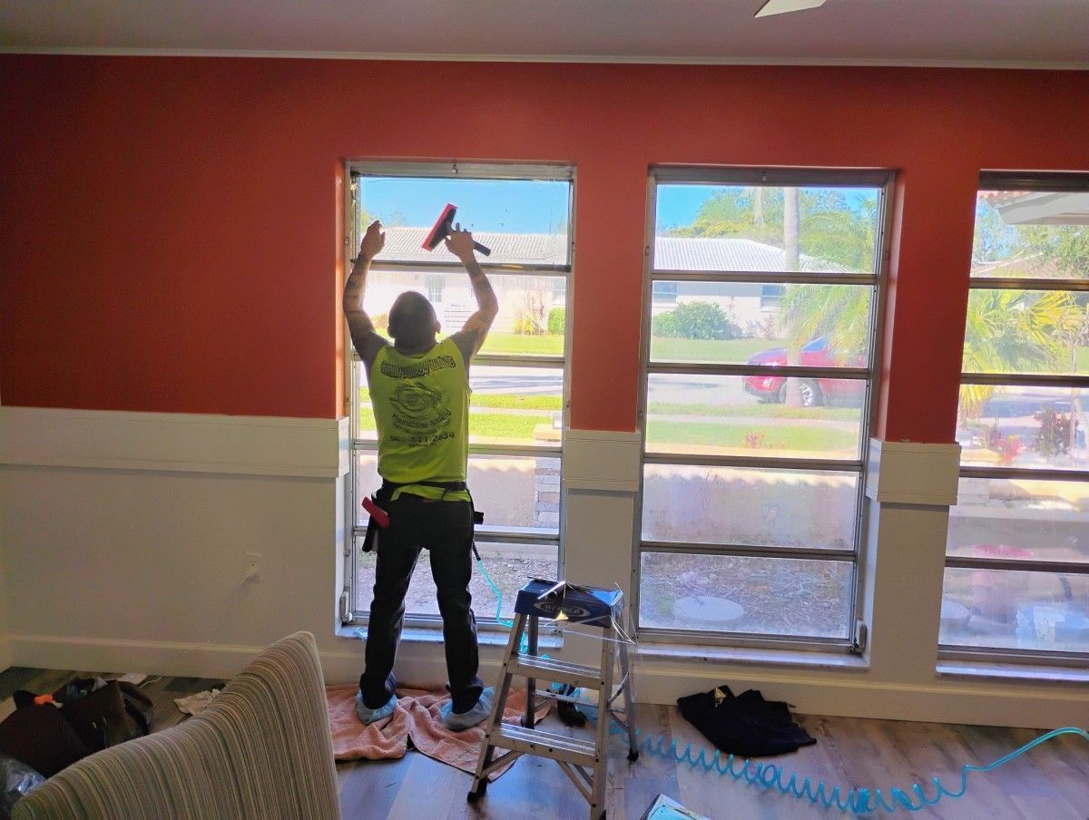 Person painting a red-and-white room, reaching up over a window with a roller brush.