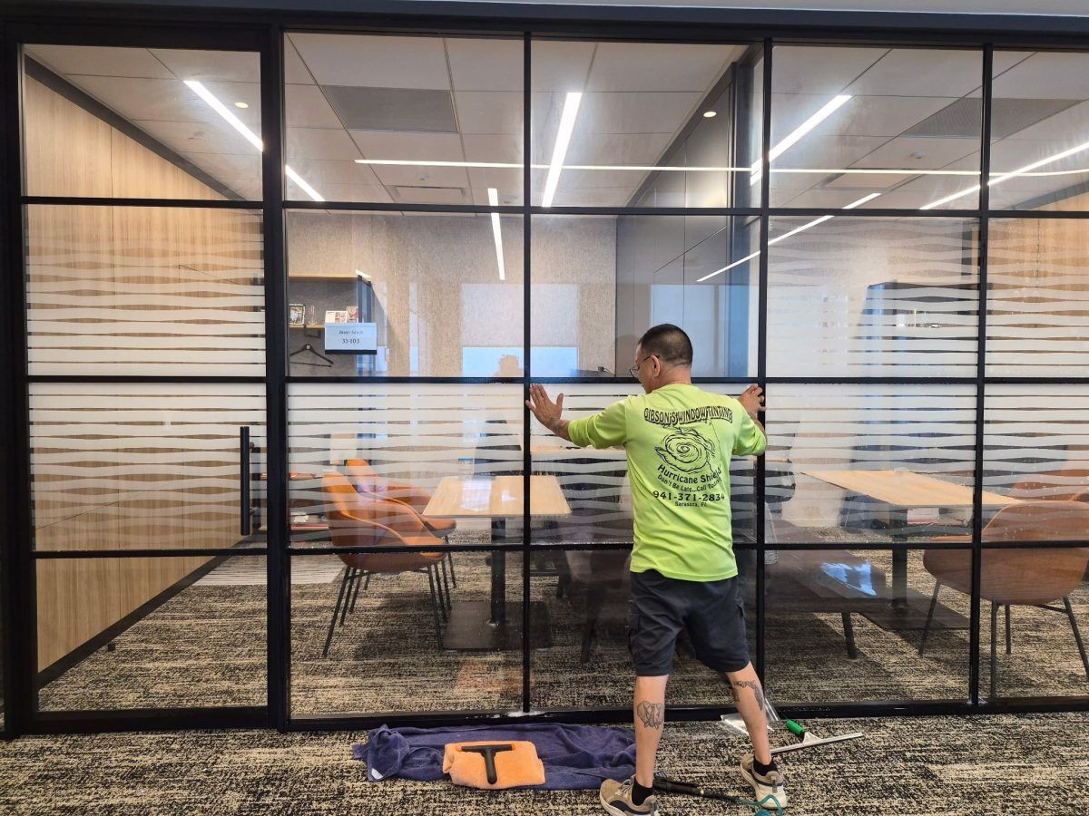 Person in a neon green shirt throwing darts in a glass-walled office game room