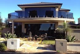 Modern two-story house with glass balconies, a covered patio, and a landscaped front entrance