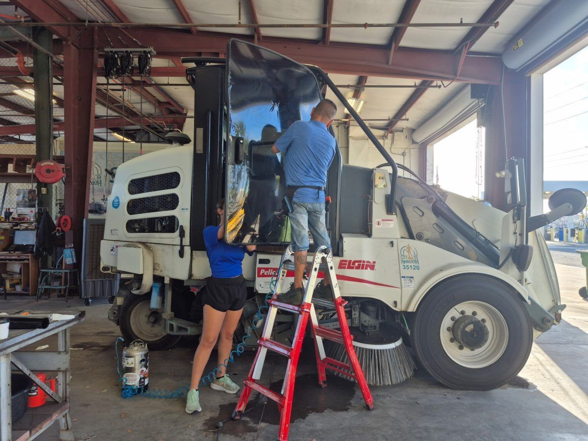 Two workers repairing a white truck inside a garage, one on a red ladder.