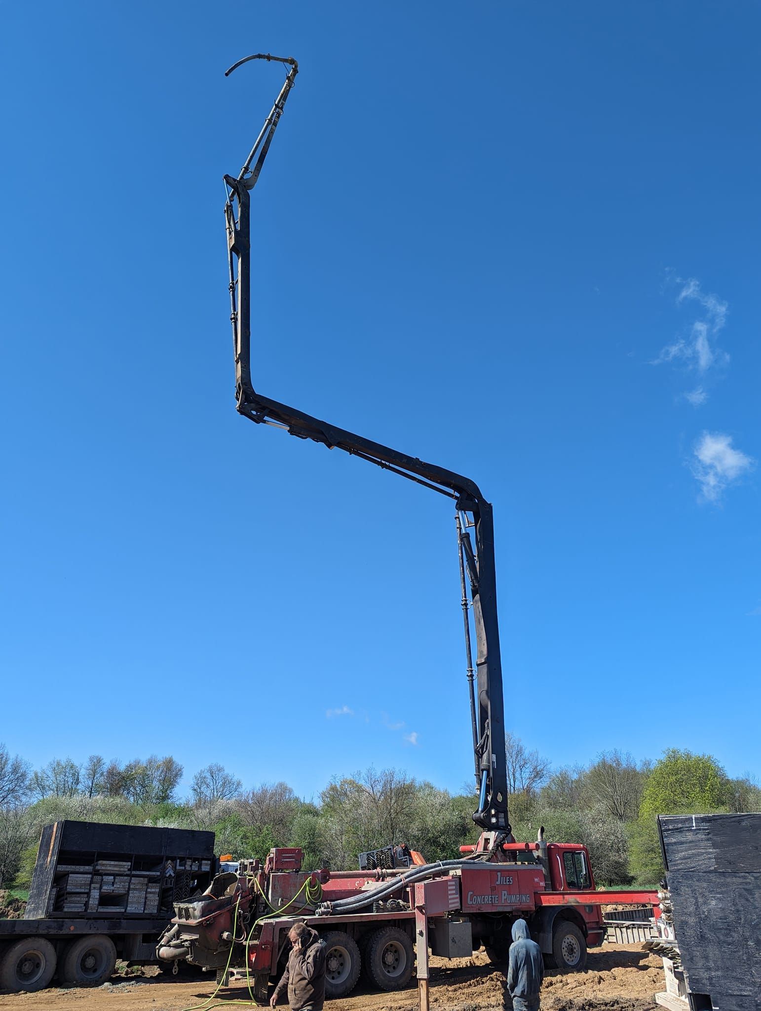 A red concrete pump truck with its long, articulated boom extended vertically into a clear blue sky at a construction site.
