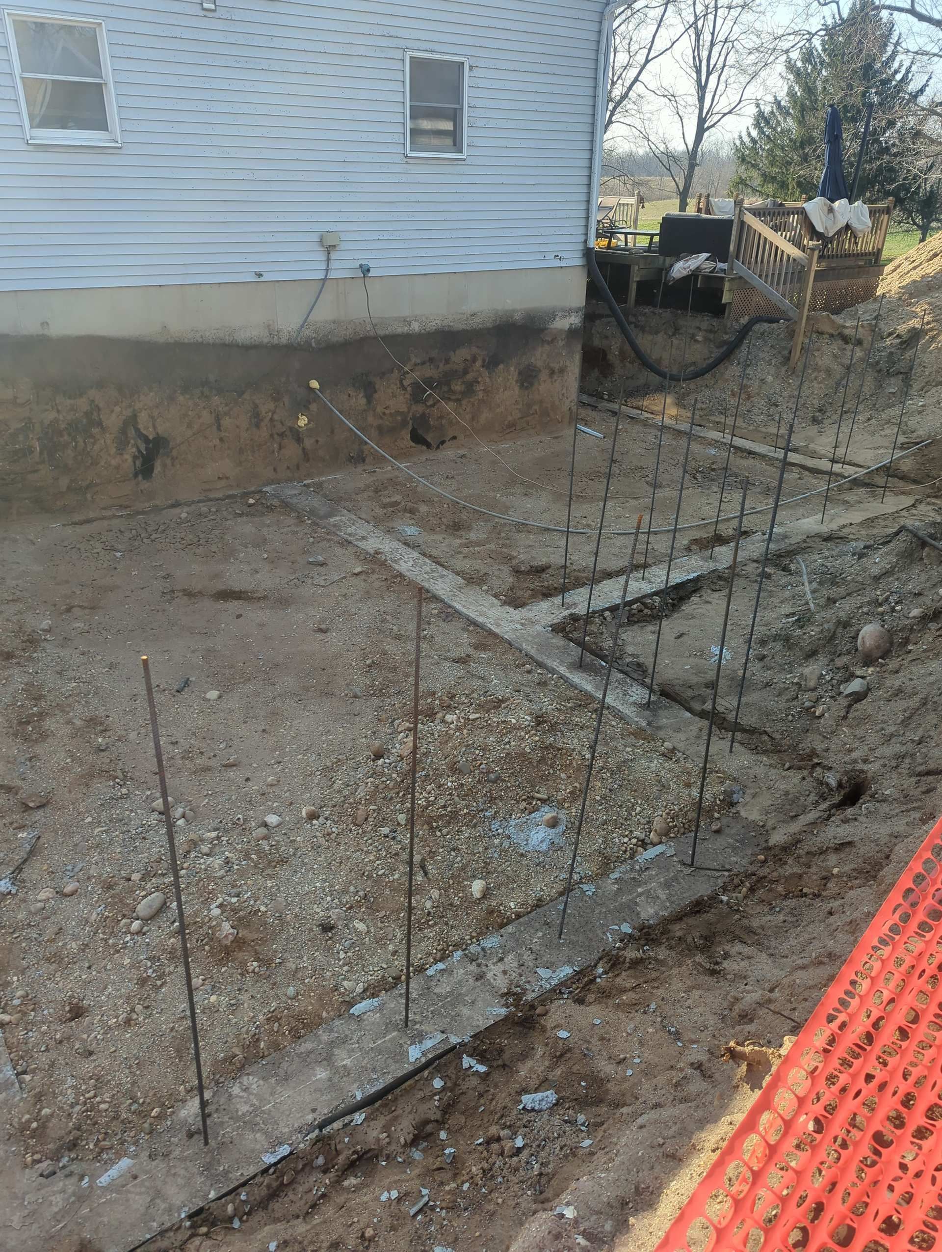 A construction site showing concrete footings with vertical rebar uprights positioned next to the side of a house.