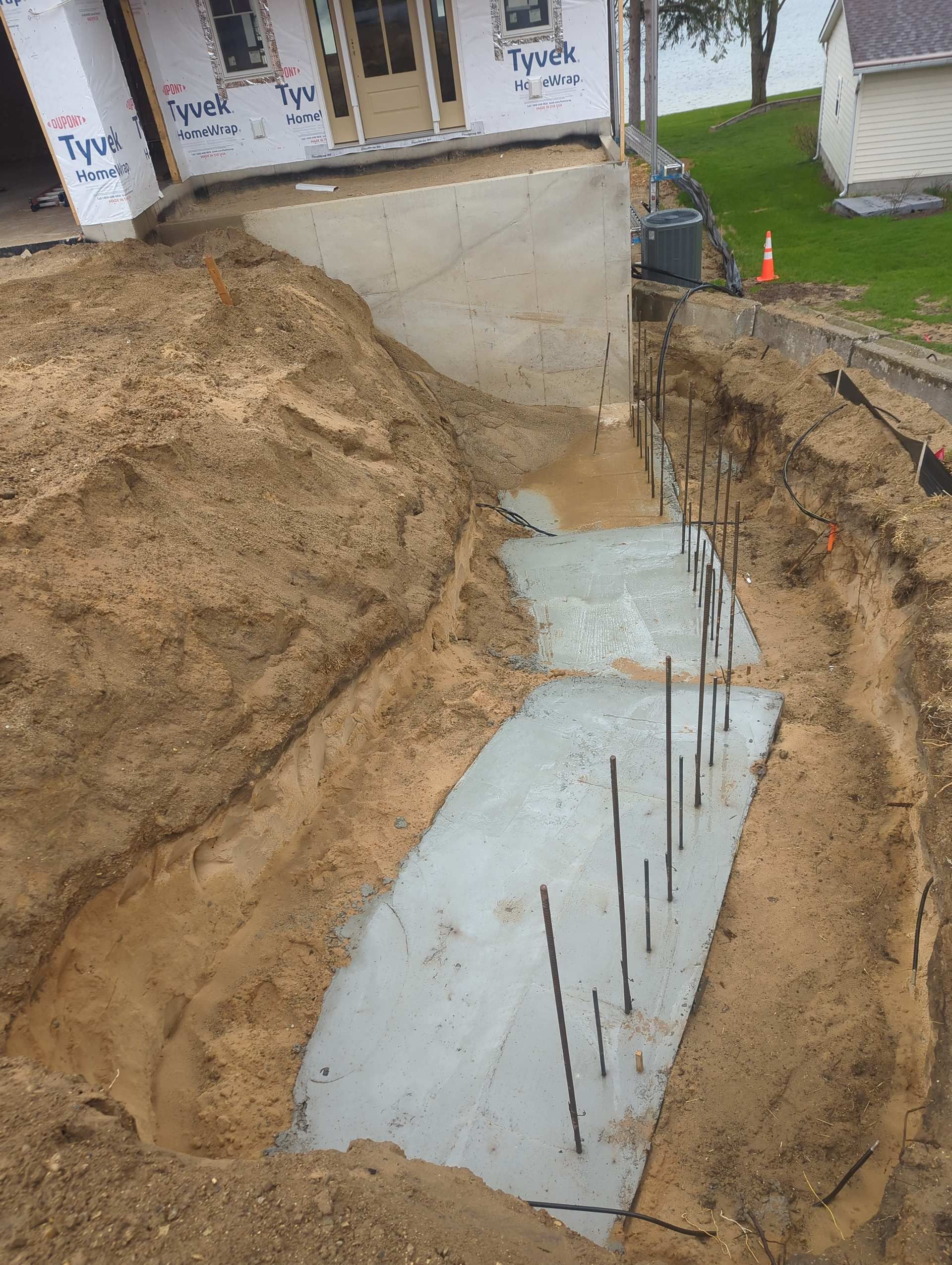 A concrete footing with vertical rebar extending from a freshly poured foundation at a residential construction site.