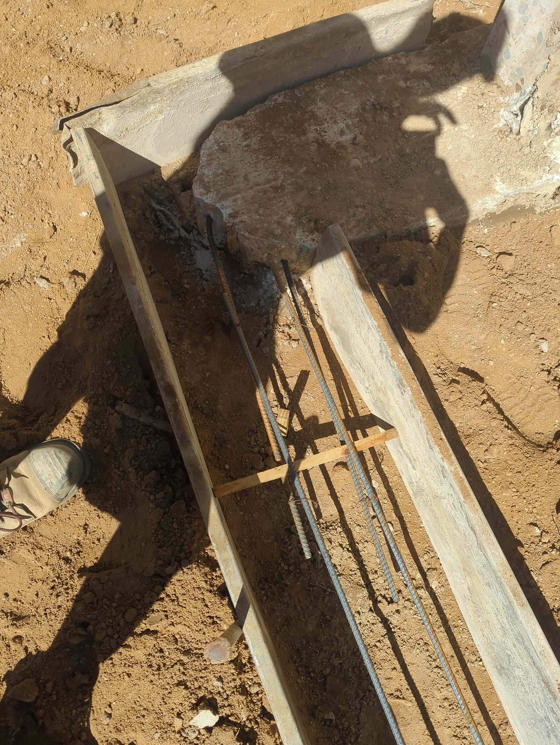 Metal formwork and steel rebar positioned in a trench on sandy ground for concrete construction.