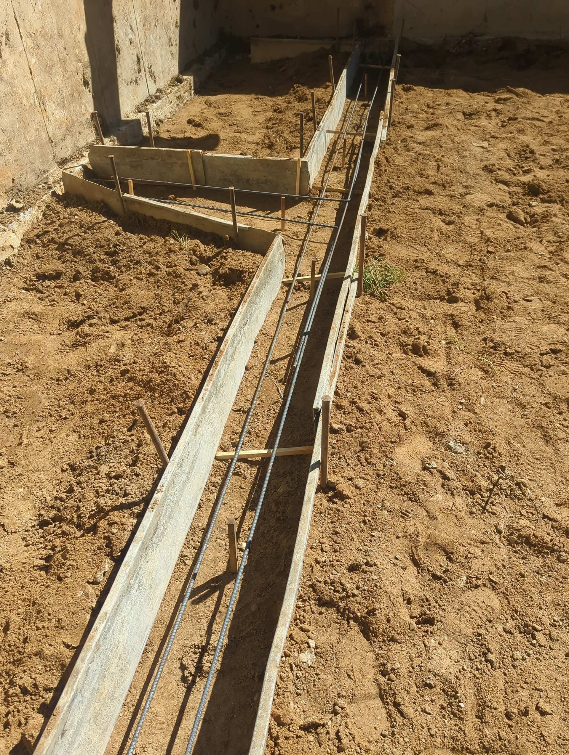 Metal formwork panels and steel rebar are set in a trench on a construction site for a concrete footing.