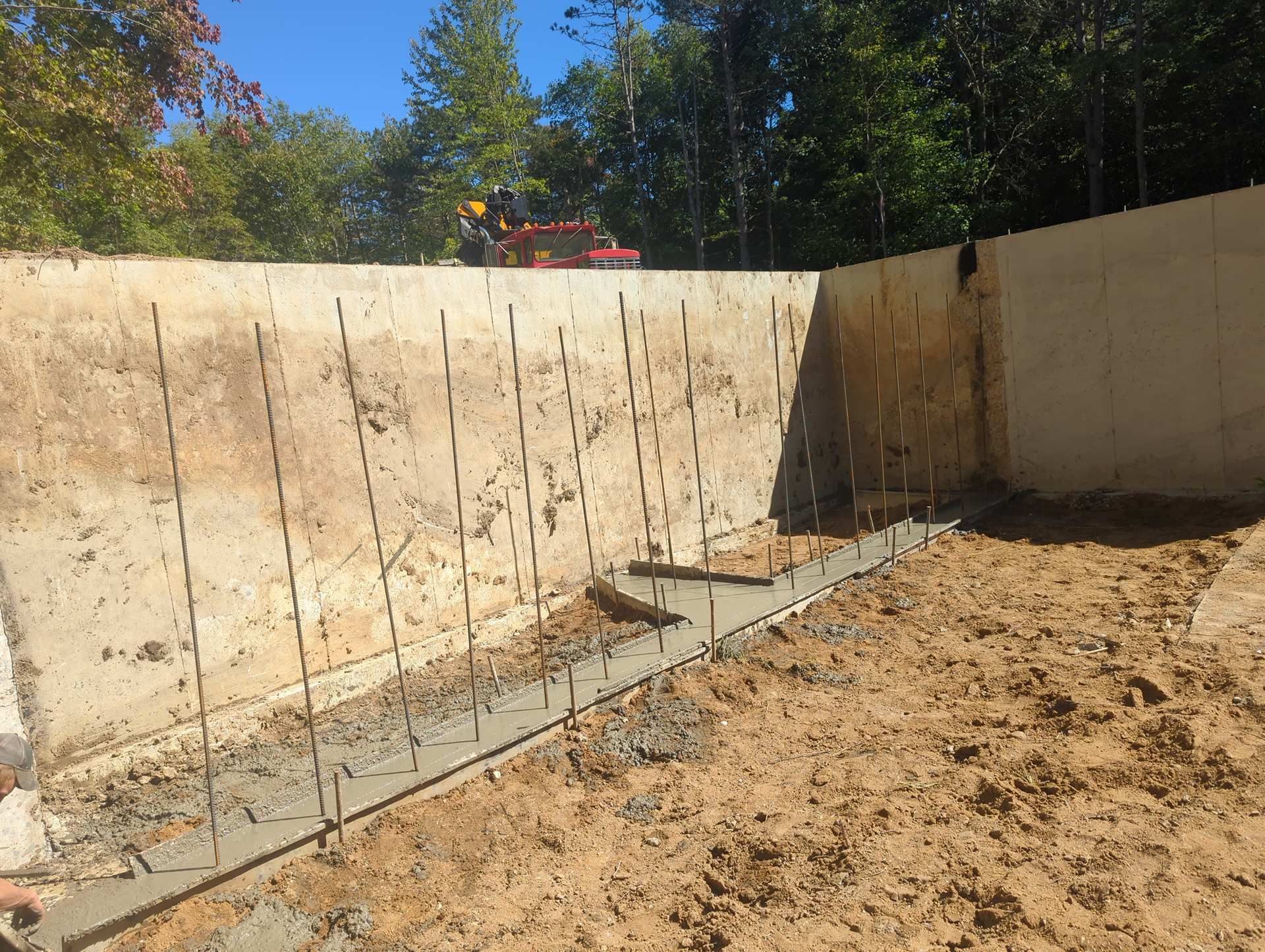 Concrete foundation walls under construction with vertical rebar sticking out of a narrow poured concrete footing.