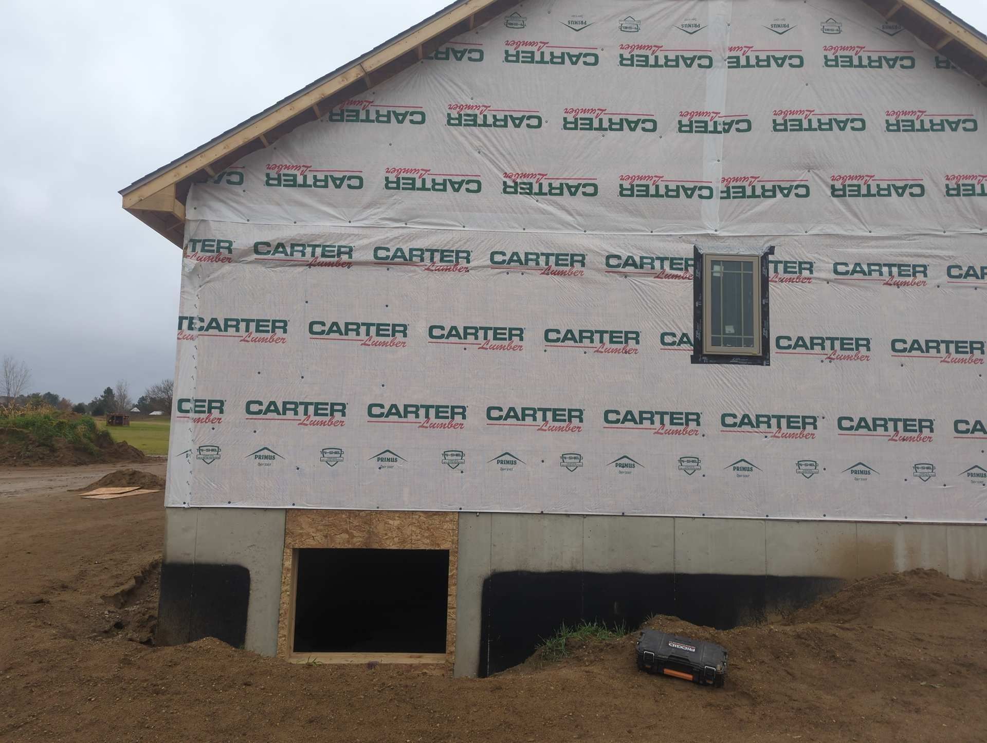 Exterior view of a residential building under construction, featuring a concrete foundation and a window-fitted wall.