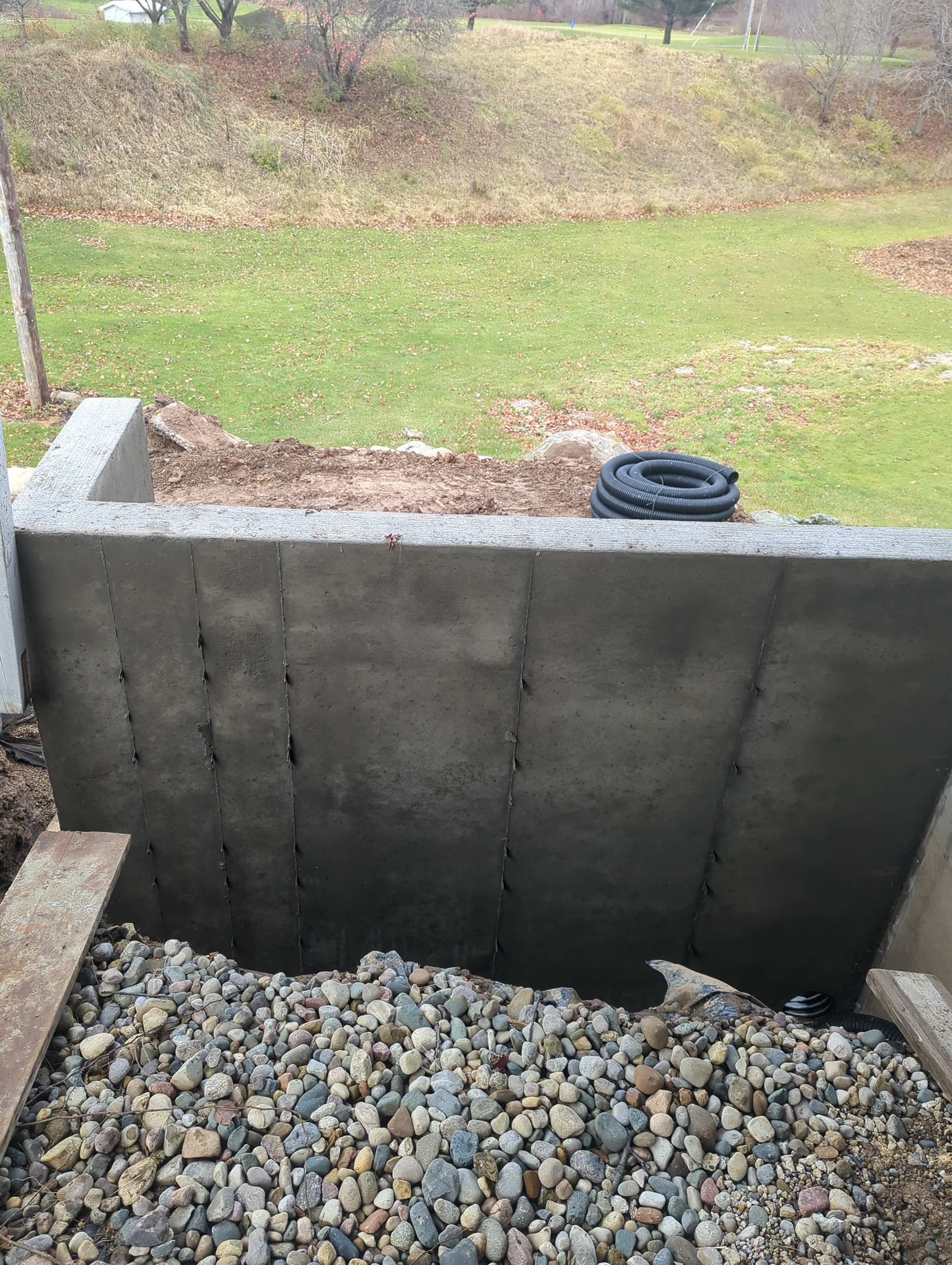 A freshly parged gray concrete basement window well wall, viewed from above, with loose gravel at the base.