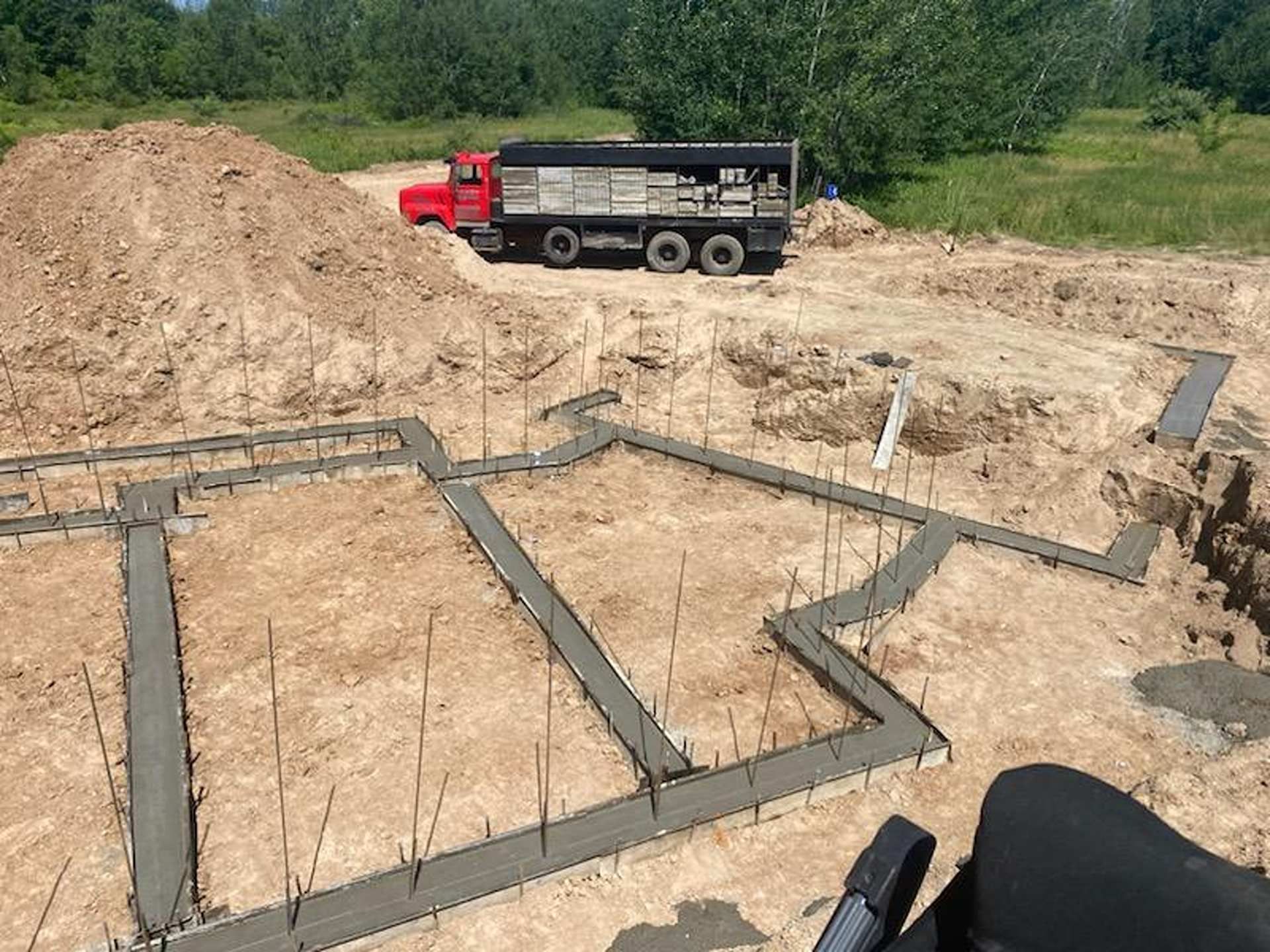 Freshly poured concrete footings form the foundation of a house at a construction site with a dump truck nearby.