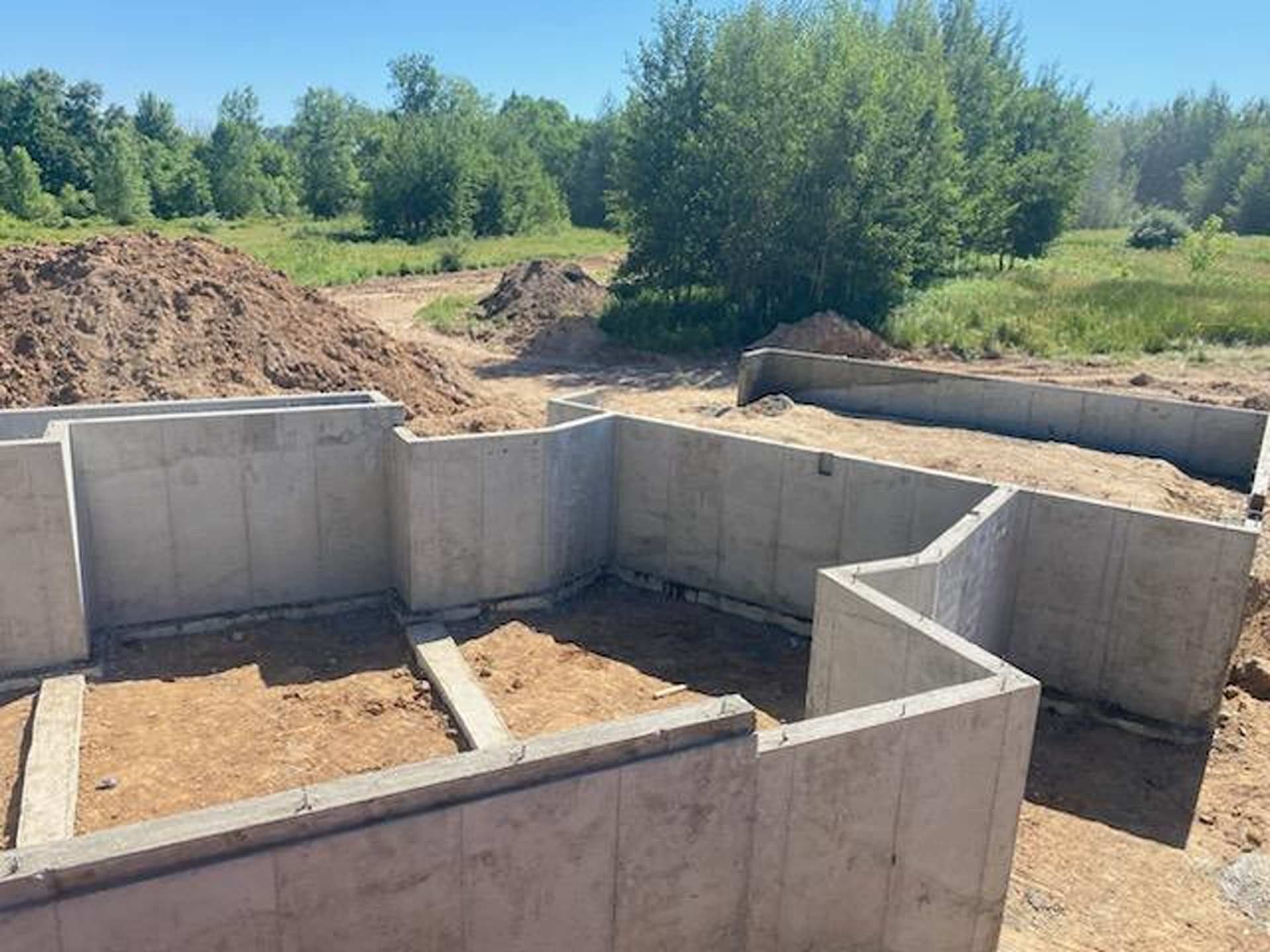 Poured concrete foundation walls for a new house under construction in a grassy, rural setting.