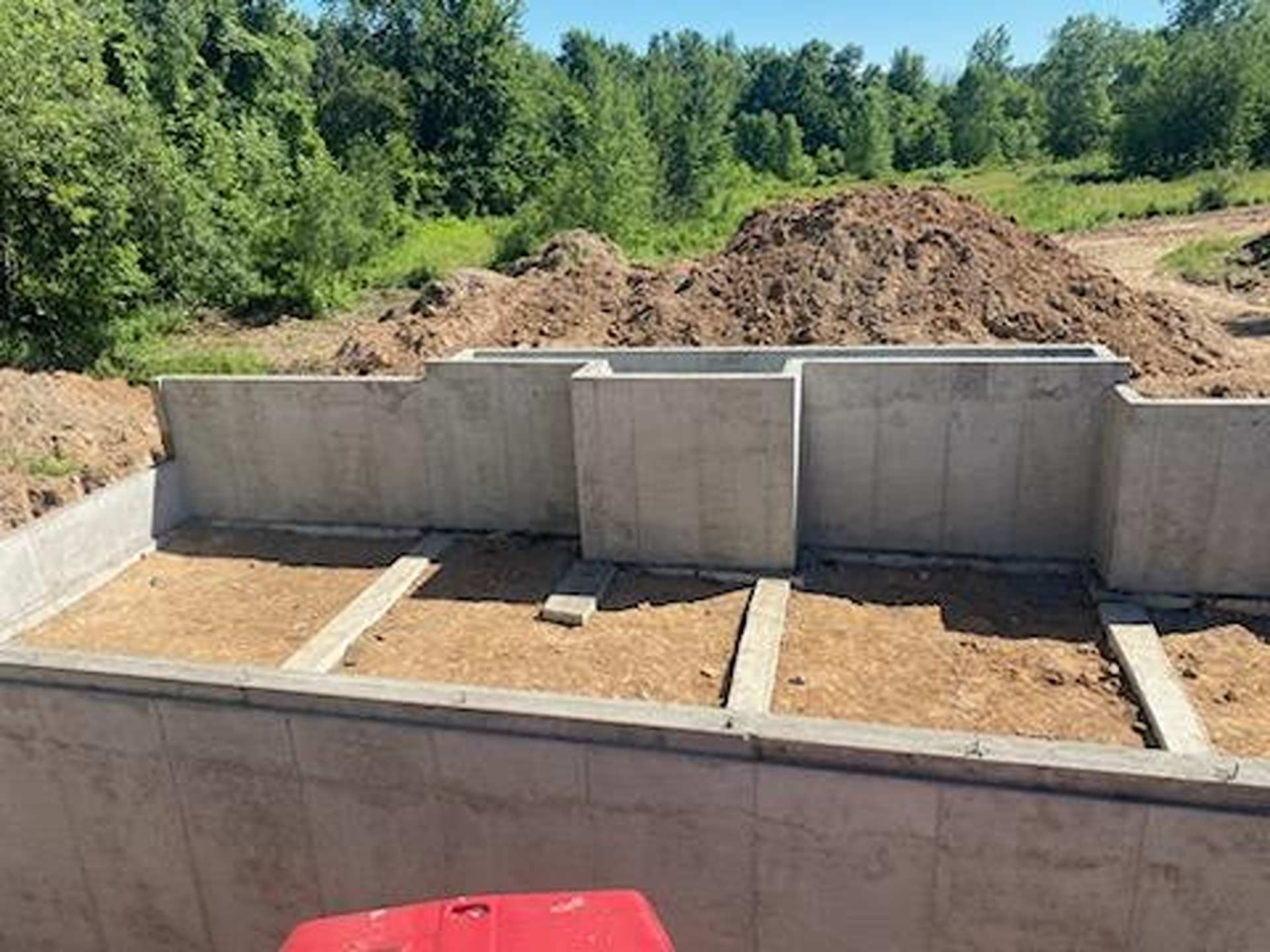 Concrete foundation walls for a new building under construction, with soil fill and wooden joists in the interior.