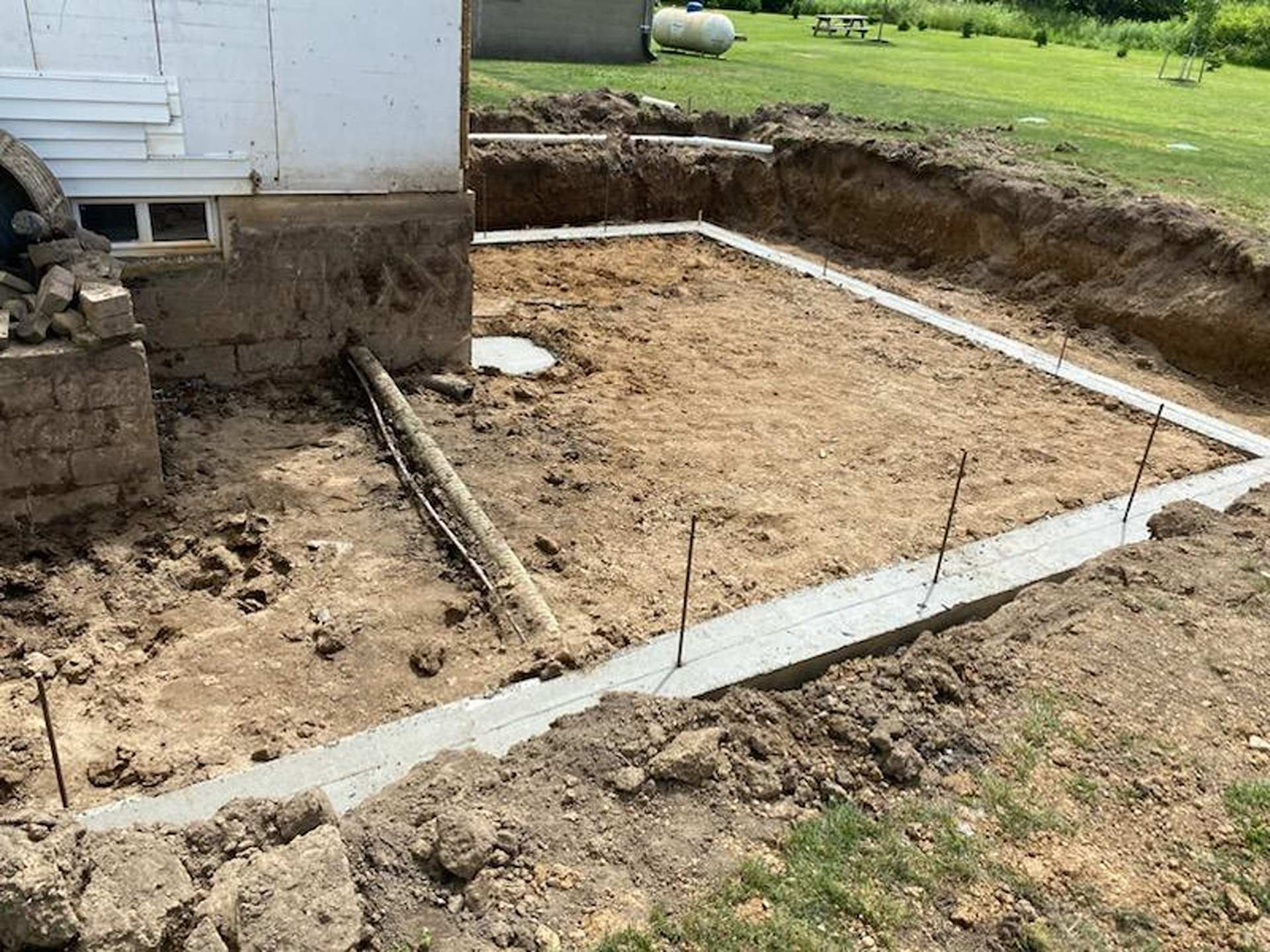 Freshly poured concrete footings for a home addition in an excavated dirt yard.