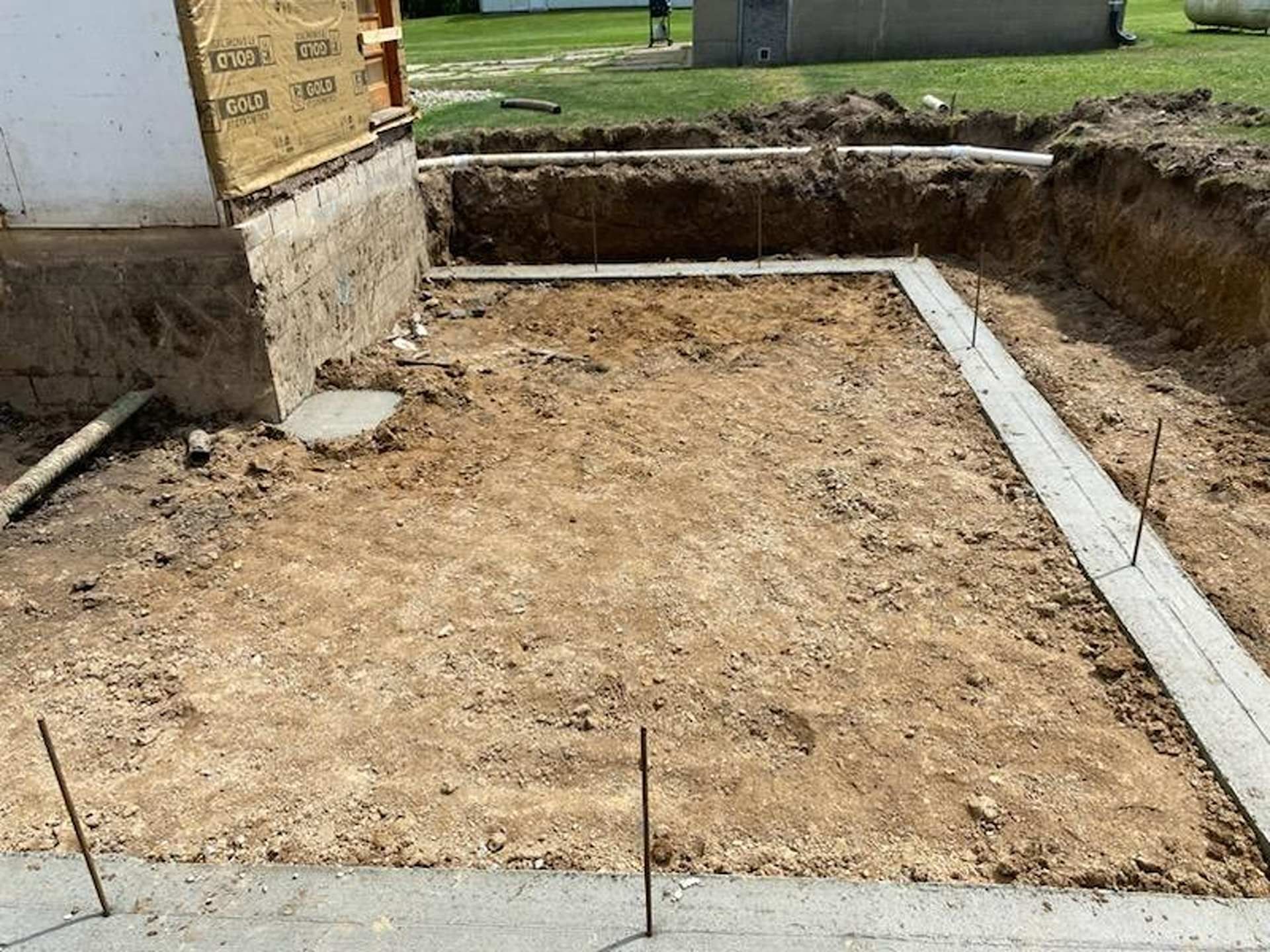 Concrete foundation footings for a home addition, viewed from above at a construction site with exposed soil.