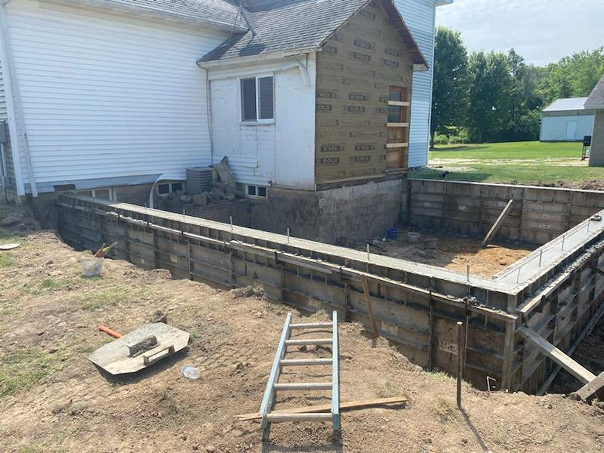 A construction site featuring a concrete foundation wall and forms for a house addition on a sunny day.