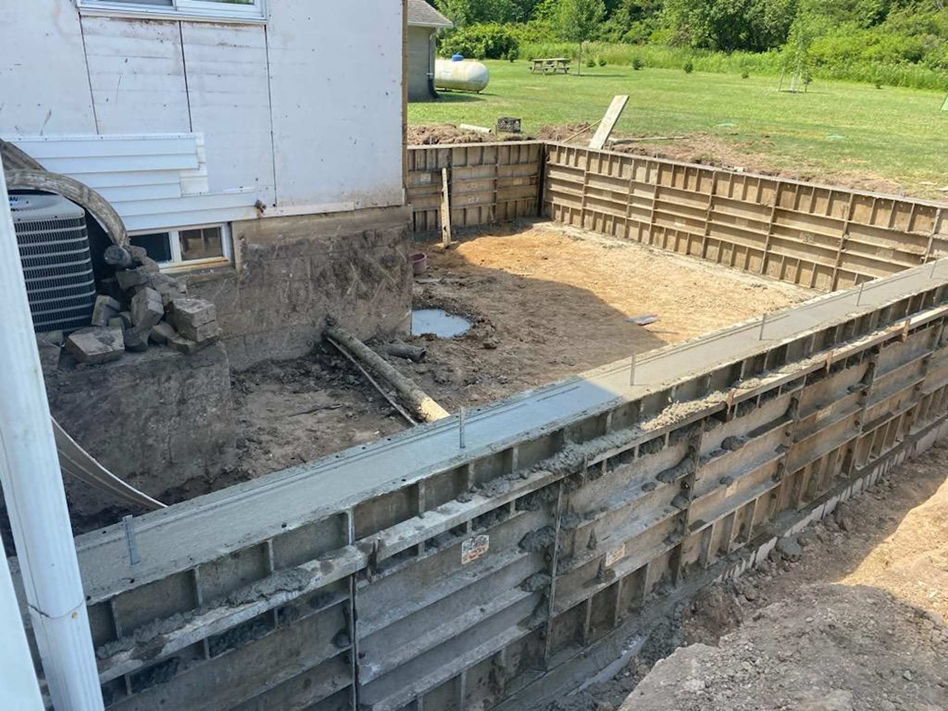 Concrete foundation forms installed around a dirt excavation site beside a white house.