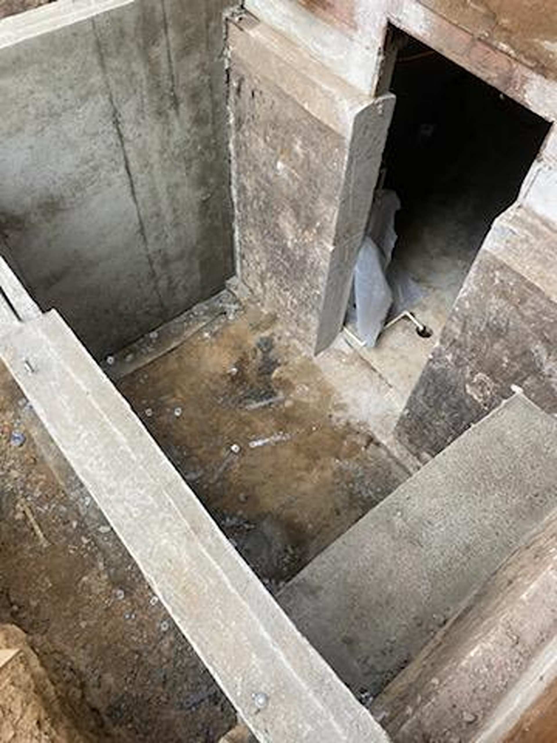 A view looking down into an unfinished concrete basement foundation with a small open doorway leading into a dark space.