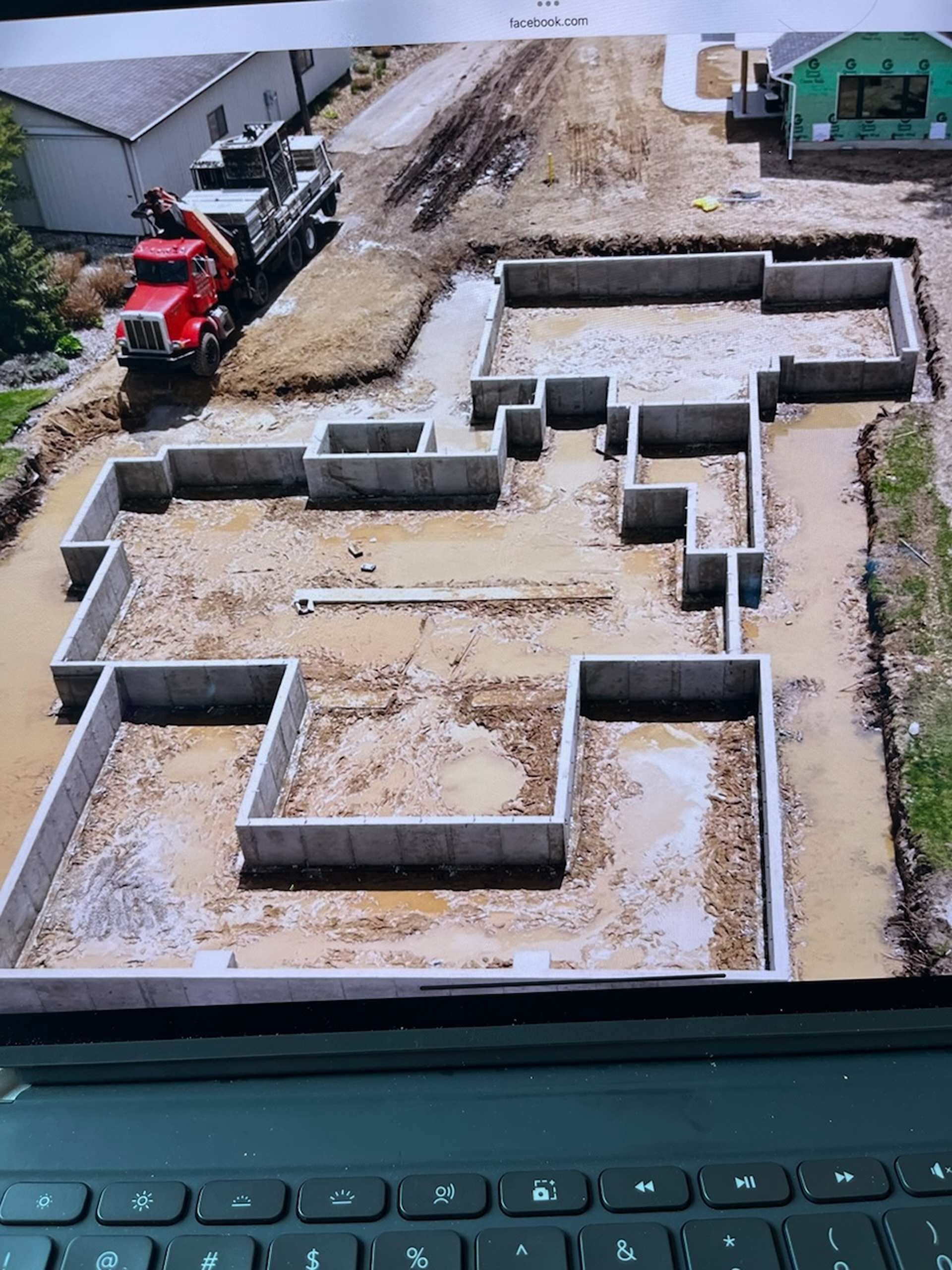 An aerial view shows the concrete foundation of a house under construction, with a red truck parked nearby.