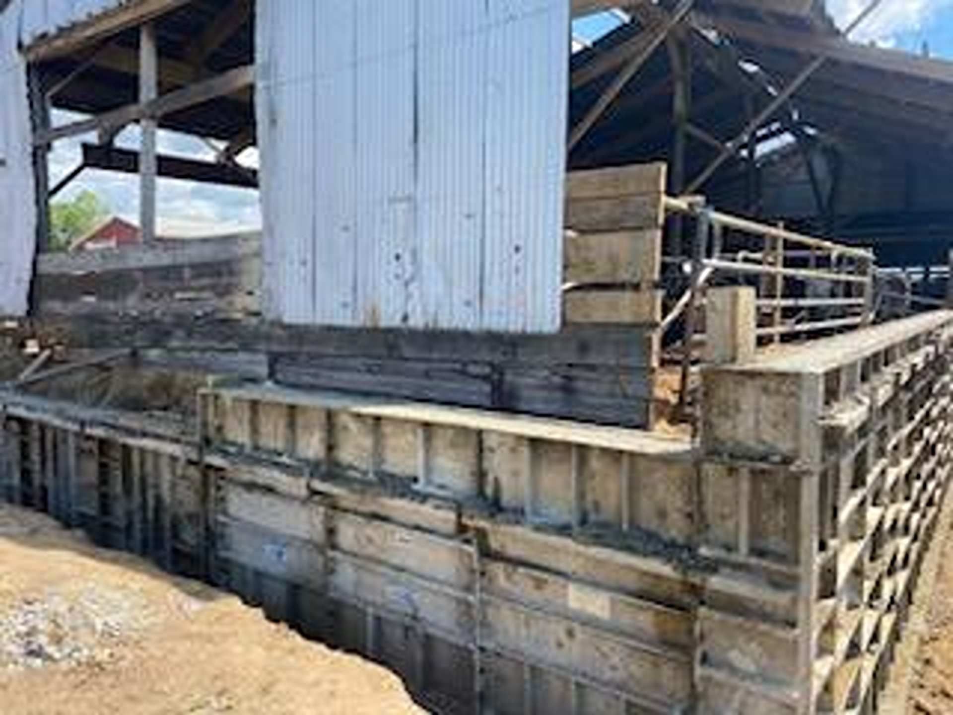 A farm structure under renovation with metal concrete forms surrounding the foundation of a wooden barn.