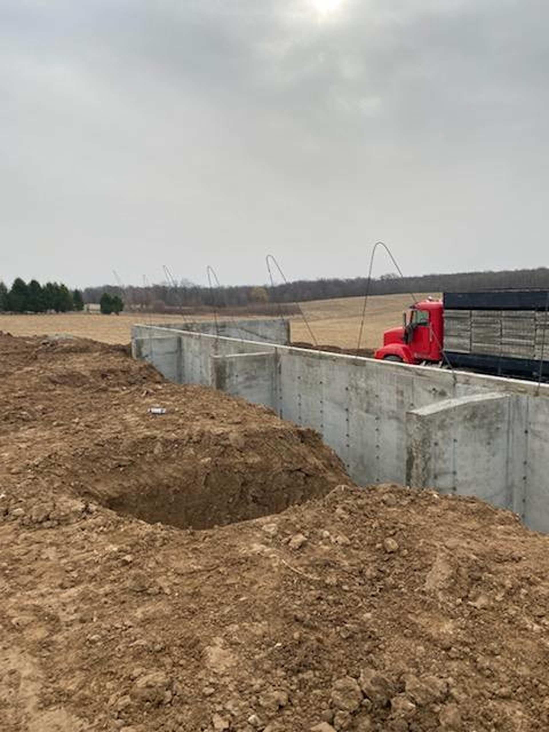 Concrete foundation walls for a building under construction, with a red truck parked nearby in a rural landscape.