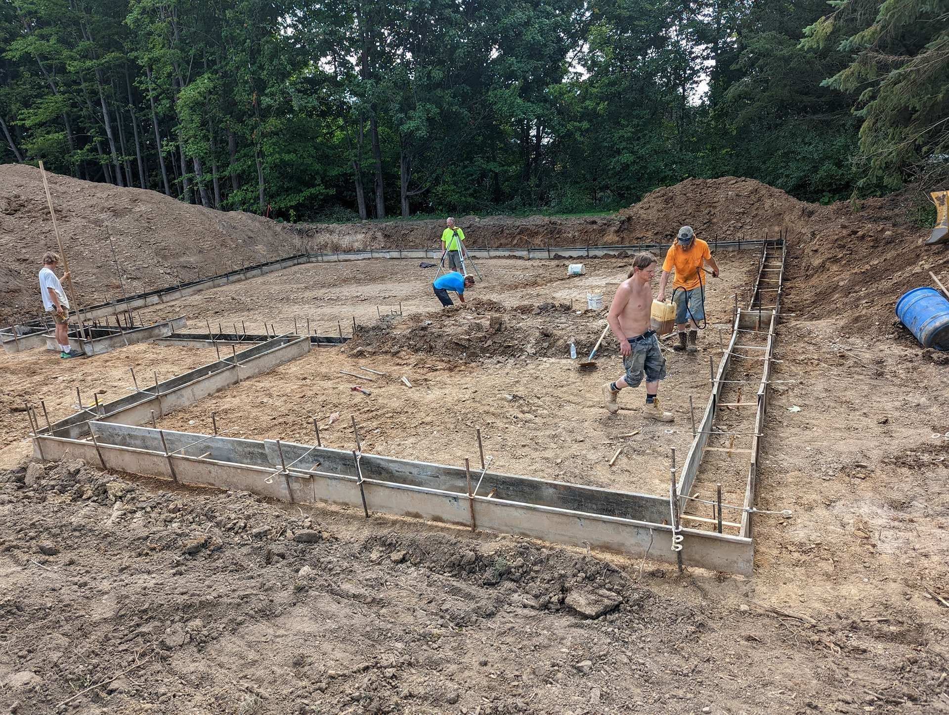 Workers in high-visibility vests prepare a wooden foundation form for concrete at a construction site.