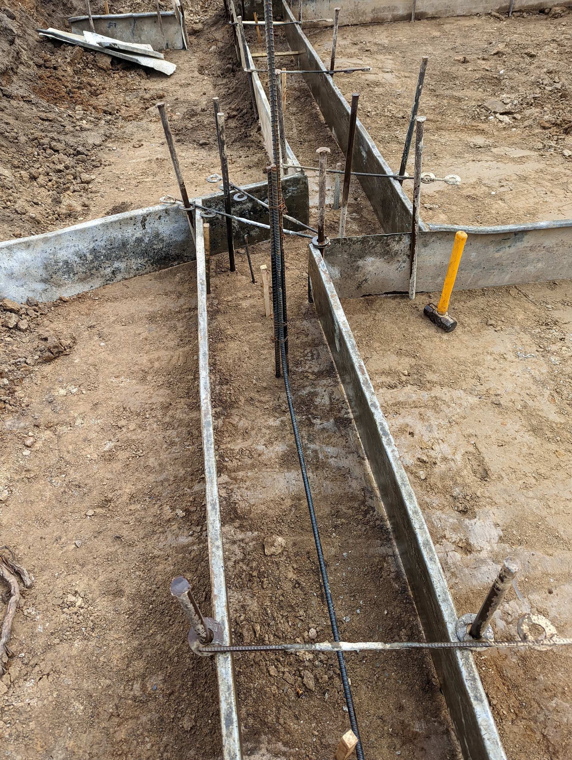 Metal concrete forms arranged in a trench for a building foundation, with visible vertical steel rebar and a yellow hammer.