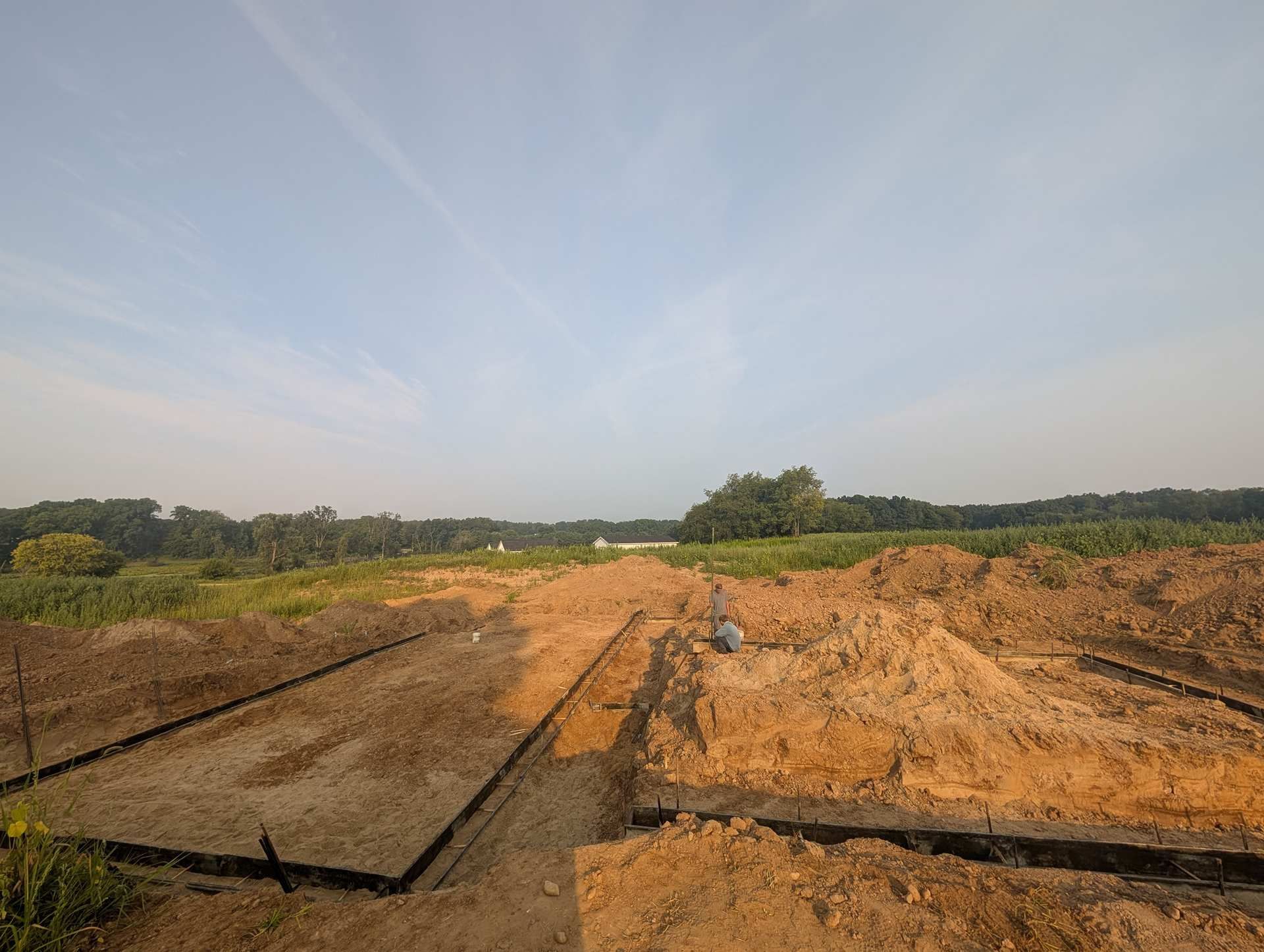 A construction site showing trenches and excavated soil foundations for a building project under a clear sky.