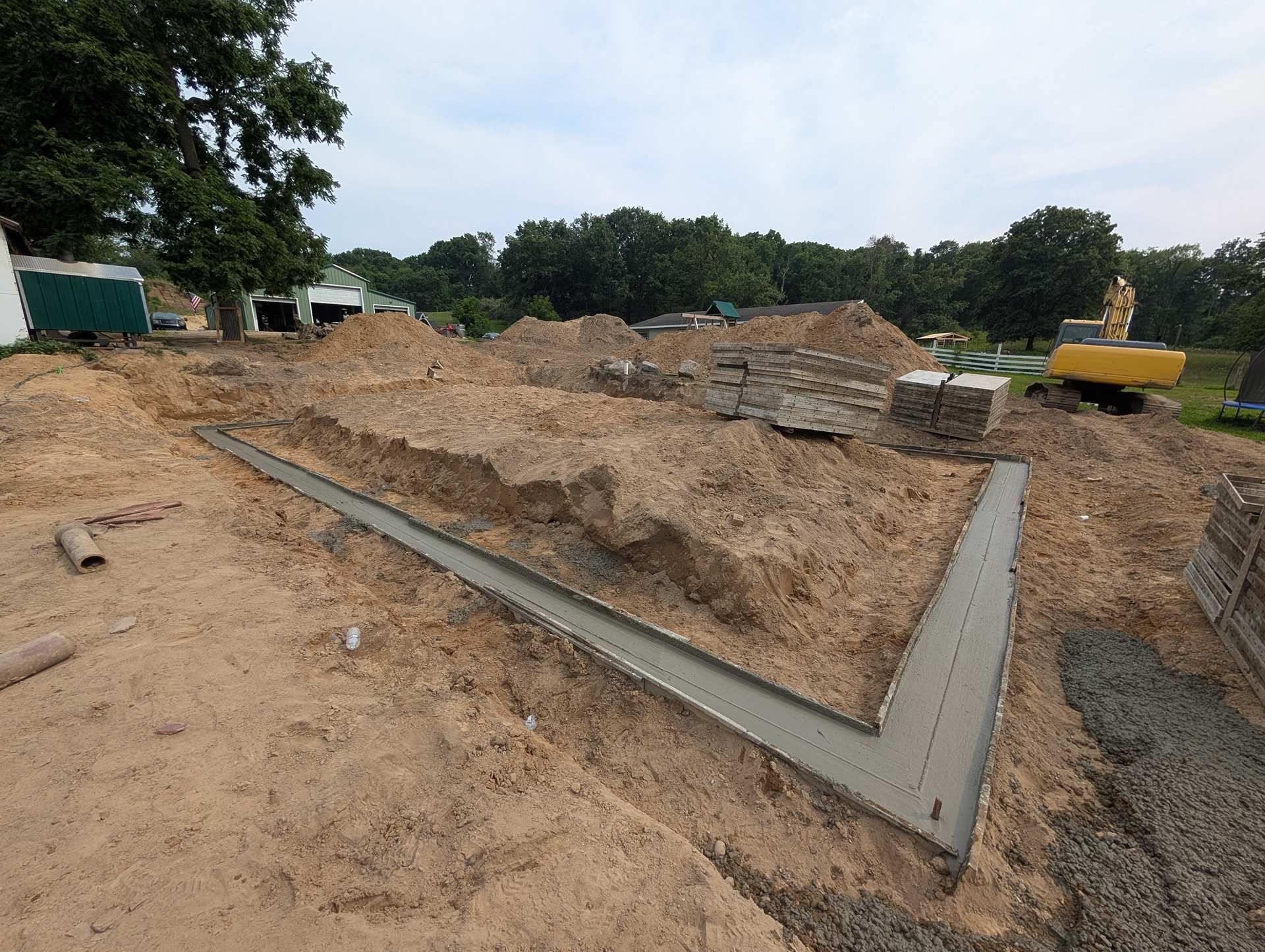 Newly poured concrete foundation footings for a building under construction, surrounded by dirt and an excavator.