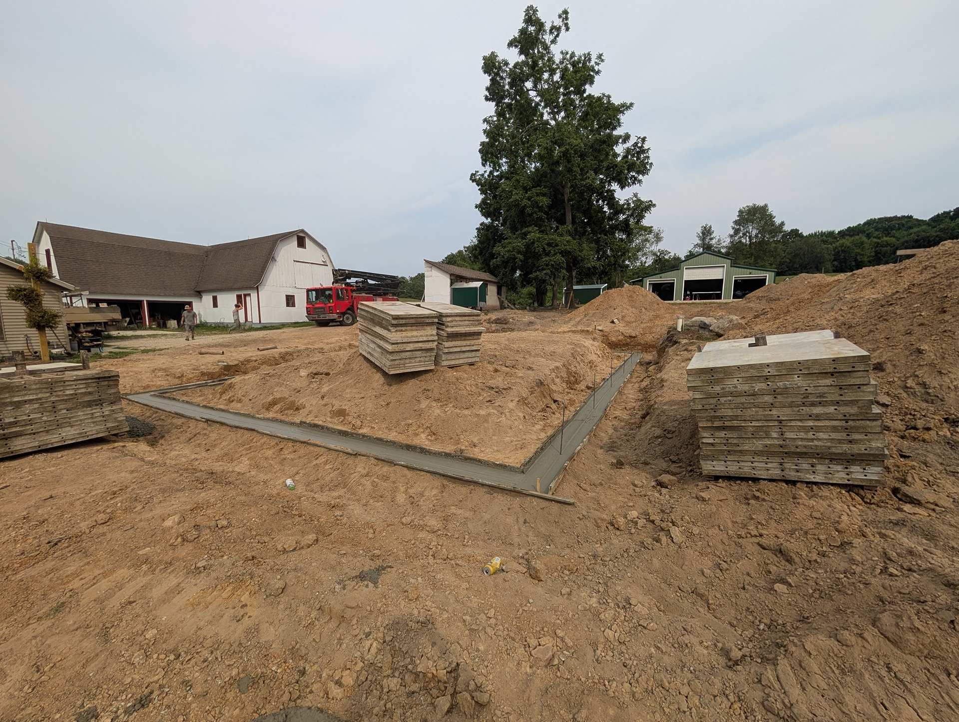 Concrete foundation footings for a building under construction, surrounded by stacks of slabs and a dirt lot.