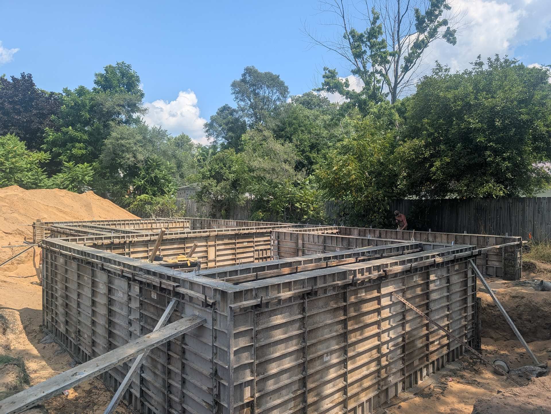 A construction site showing metal concrete forms installed for a foundation on a sunny day with trees in the background.