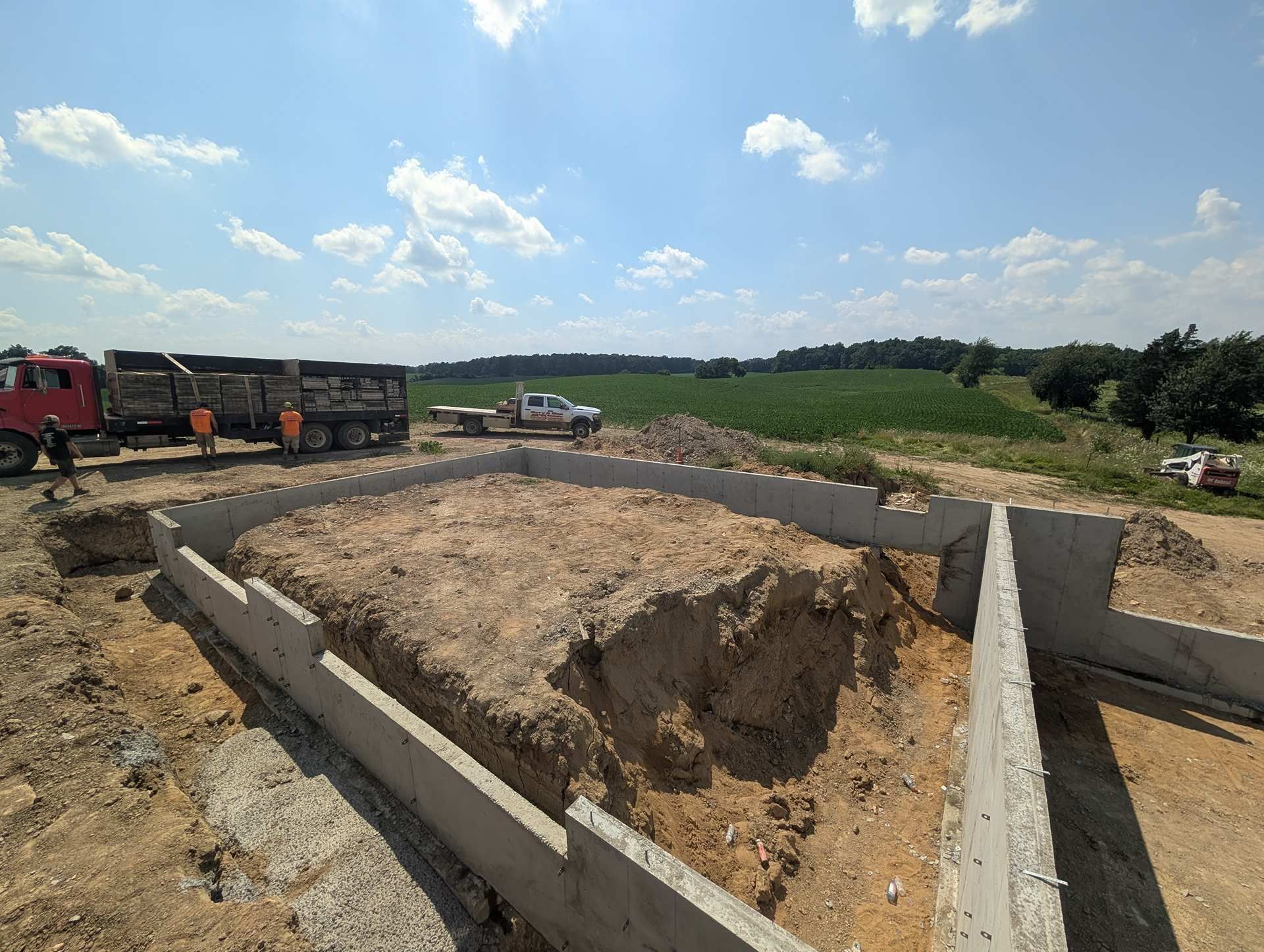 Concrete foundation walls for a building under construction on a sunny, rural job site with trucks nearby.